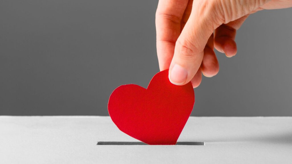 Hand gibt ein rotes Herz in eine Spendenbox